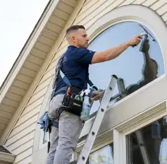 Professional window cleaner on a ladder using a squeegee to clean an exterior arched window, New Orleans, LA.